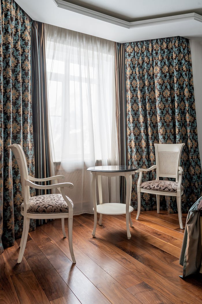 Vintage interior design with elegant chairs and table by a window with draped curtains.