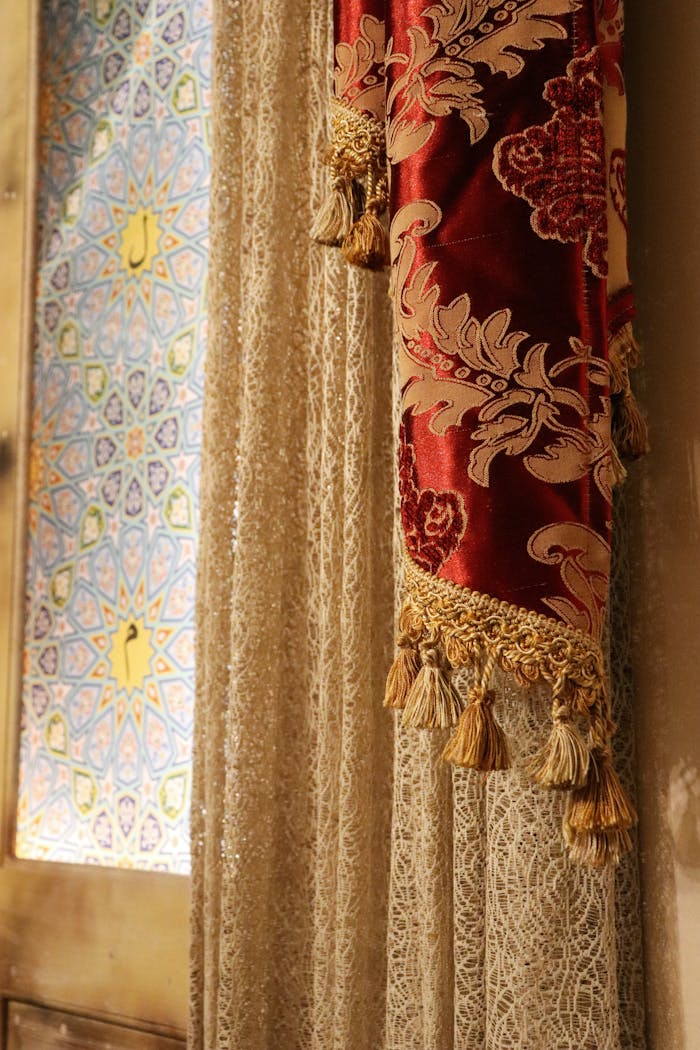 Elegant lace curtain with ornate red fabric beside colorful stained glass window.