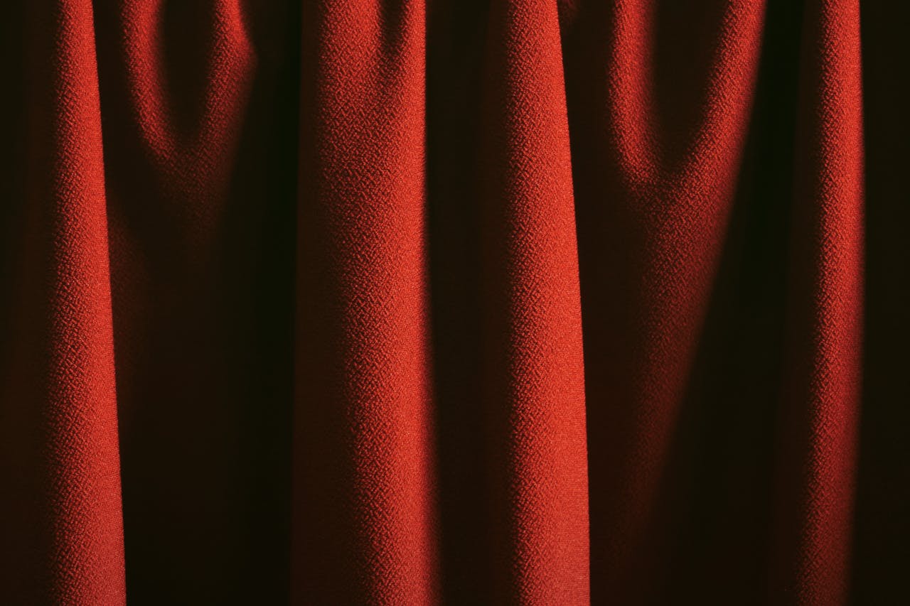 A classic red curtain with a rich texture and elegant folds in soft lighting.
