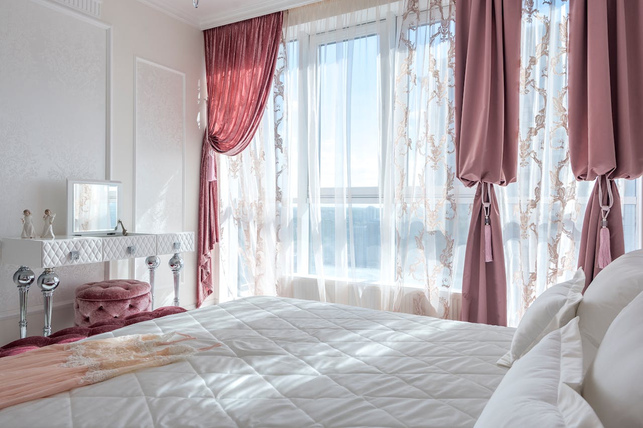 Cozy and elegant white and rosy bedroom with comfortable bed and draped curtains